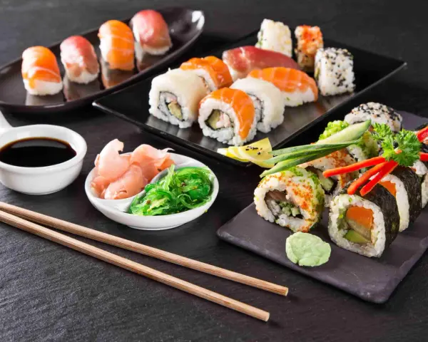 Pyszne sushi, w tym uramaki, z łososiem i awokado, podane z imbirem, wasabi i sosem sojowym.