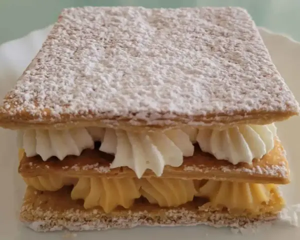 Delicioso milhojas de crema, con capas crujientes de hojaldre y rellenos de crema pastelera y nata montada, espolvoreado con azúcar glas.