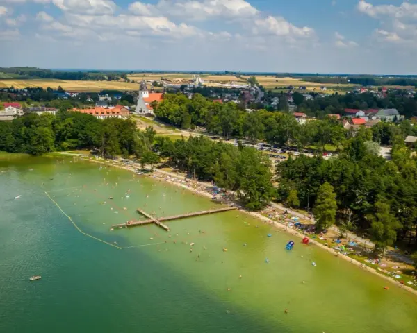 Letnie popołudnie nad jeziorem wielewskim. Tłumy plażowiczów, kąpielisko z pomostem i urokliwa miejscowość w tle.