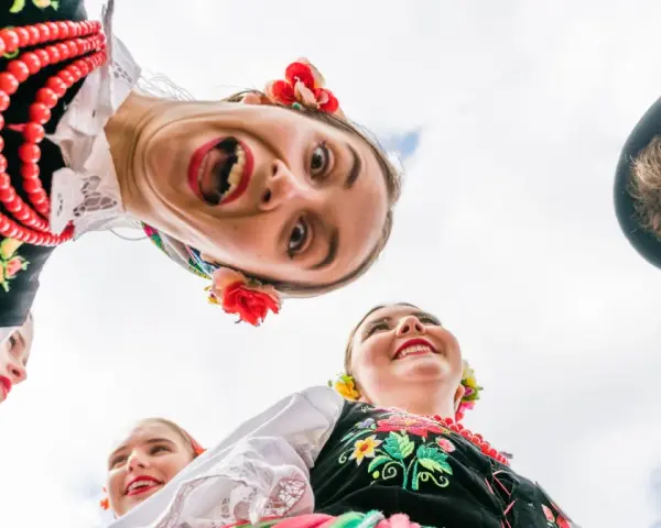 Uśmiechnięci młodzi ludzie w barwnych strojach ludowych, żywa ludowa twórczość artystyczna.