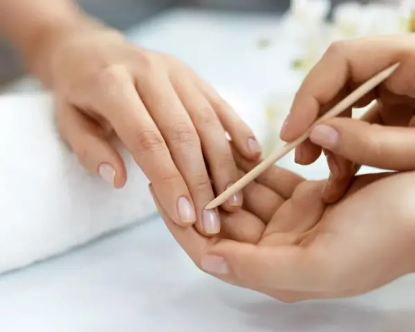 Delikatne dłonie poddawane zabiegowi manicure biologiczny. Skórki są starannie odsuwane patyczkiem, przygotowując paznokcie do dalszej pielęgnacji.