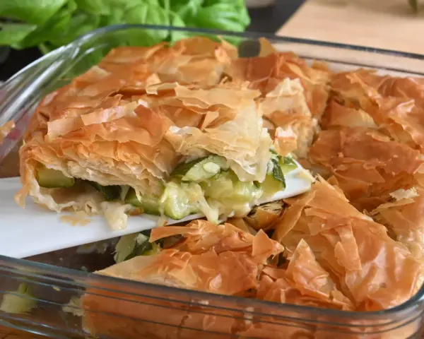 Una fetta di torta salata con zucchine, con croccante pasta sfoglia dorata e ripieno filante.