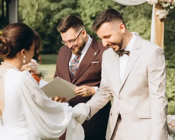 Uroczystość ślubna: panna młoda w białej sukni, pan młody w jasnym garniturze i urzędnik. To piękny ślub humanistyczny, a nie tylko cywilny.