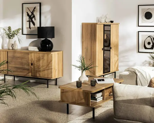 Drewniane meble i subtelne dodatki tworzą przytulną atmosferę w stylu hygge. Wazon z gałązkami i czarna lampa dodają elegancji.