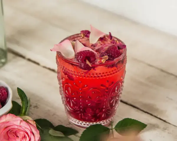 Orzeźwiający drink z malinami, ozdobiony płatkami róż i świeżymi malinami. Idealny na letnie popołudnie.
