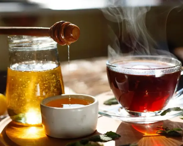 Une cuillère en bois verse du miel doré dans une tasse de thé fumante. Un délice réconfortant de miel dans eau chaude.