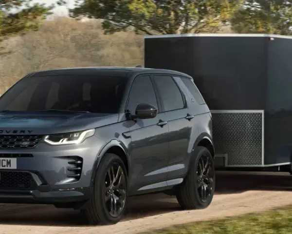 Szary Land Rover Discovery Sport z przyczepą o masie 2000 kg jedzie po leśnej drodze.