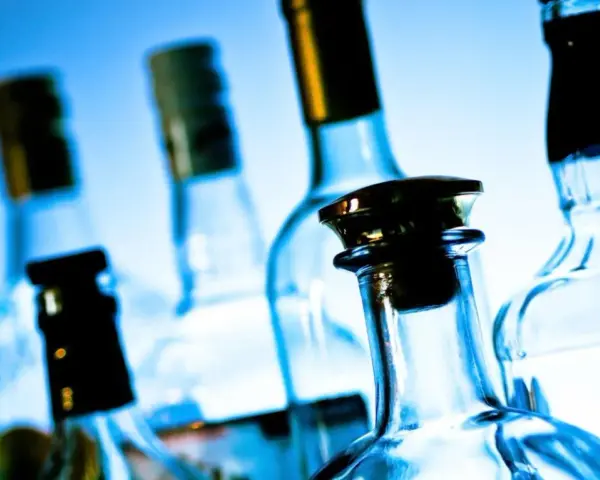 Kilka szklanych butelek alkoholu na niebieskim tle.