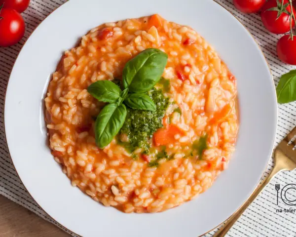 Pyszne risotto z pomidorami, udekorowane bazylią i pesto, czeka na talerzu. Obok świeże pomidorki i złoty widelec.