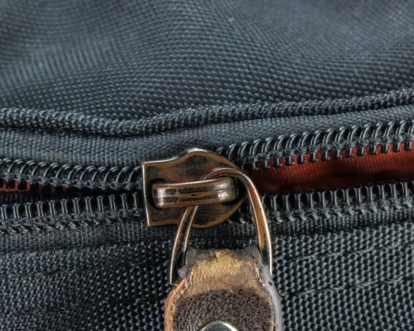 Nahaufnahme eines Reißverschlusses an einer schwarzen Tasche. Der Schieber ist aus Metall und leicht abgenutzt, was auf die Notwendigkeit hinweist, den Reißverschluss zu reparieren.