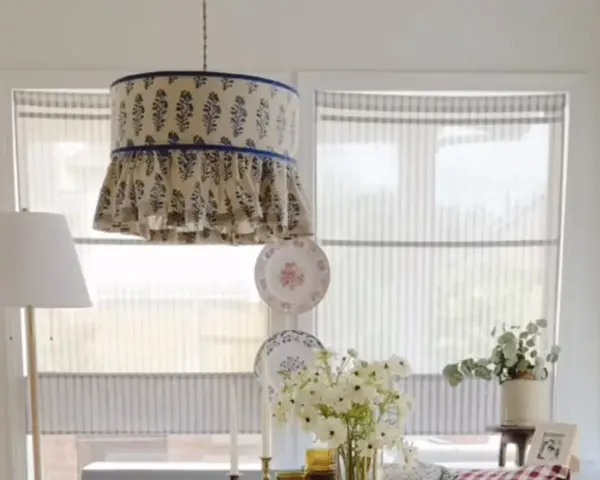Un abat-jour suspendu avec un motif floral bleu et des volants, une excellente idée déco abat jour. Des assiettes décoratives et des fleurs complètent la scène.