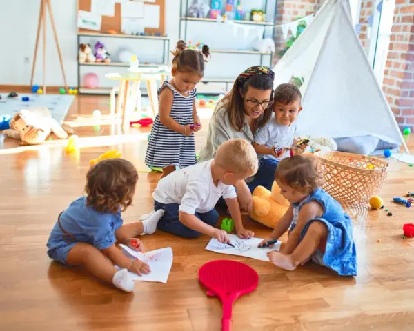 Niania w Warszawie, opiekująca się grupą dzieci, które rysują na podłodze. Zastanawiasz się, ile zarabia niania w Warszawie?