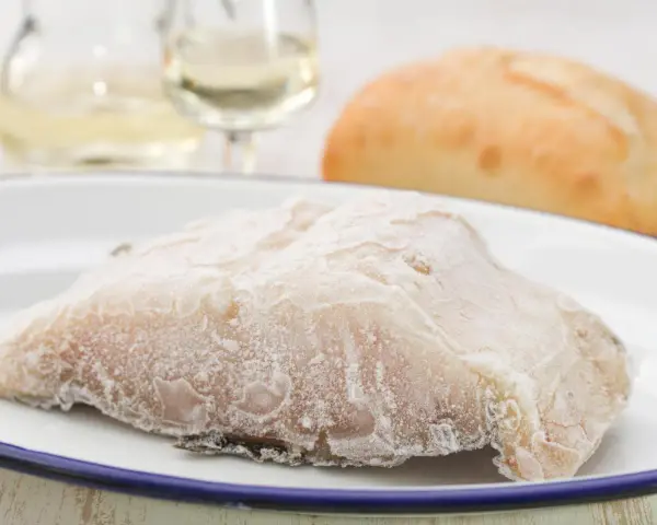 Un trozo de pescado en blanco, escarchado, listo para cocinar. Acompañado de pan y vino blanco.