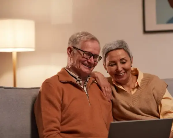 Uśmiechnięta para seniorów przegląda coś na laptopie. Zastanawiają się, czy zwolnienia lekarskie mają wpływ na wysokość emerytury.