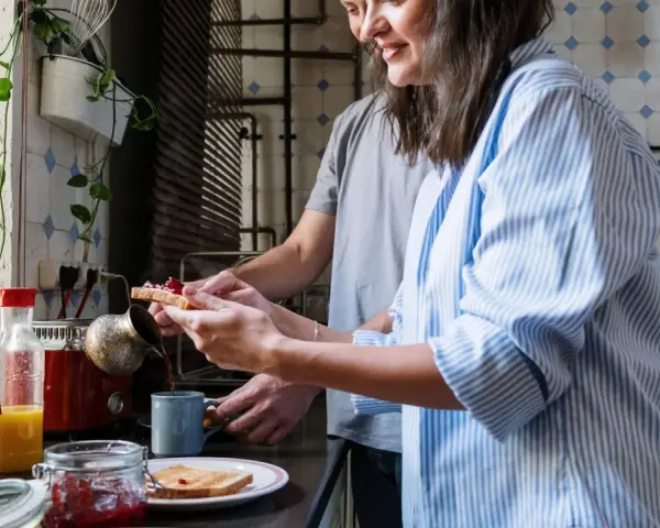 Pareja preparando el desayuno, tostadas con mermelada y café. Un momento de "bonjour" en francés para empezar el día.