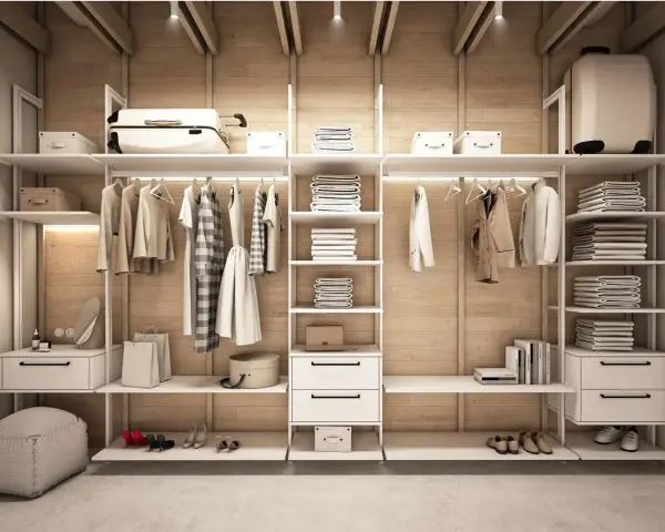 Minimalistyczna garderoba w stylu basic. Ubrania wiszą na wieszakach, stosy ręczników i pościeli na półkach. Wygodny puf i eleganckie buty dopełniają całość.