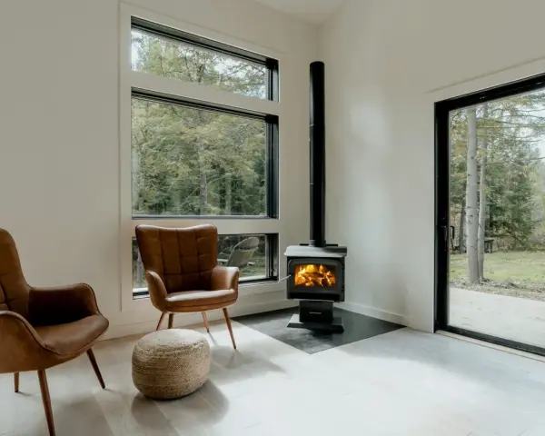 Un poêle à granule appartement, avec deux fauteuils en cuir marron et une vue sur la forêt.