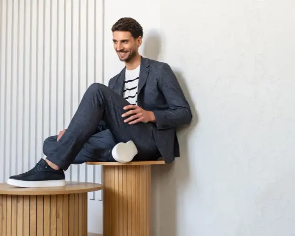 Uśmiechnięty mężczyzna w granatowym garniturze i białej koszulce w paski, idealny przykład dress code smart casual.