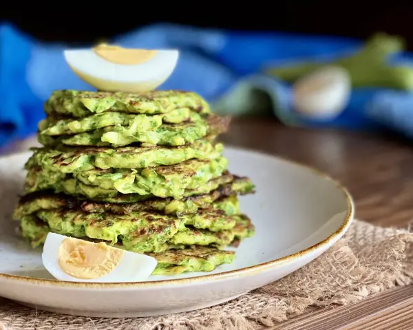 Pila di rosti di zucchine dorati, guarnita con spicchi di uovo sodo. Un piatto leggero e gustoso, perfetto per ogni pasto.