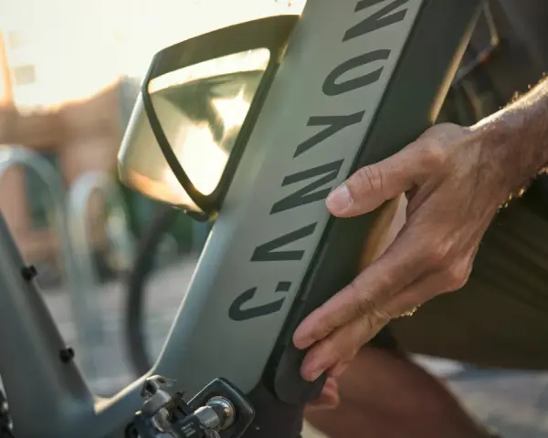 En hand justerar en elcykel. Solen skiner genom ett fönster på cykelns ram.
