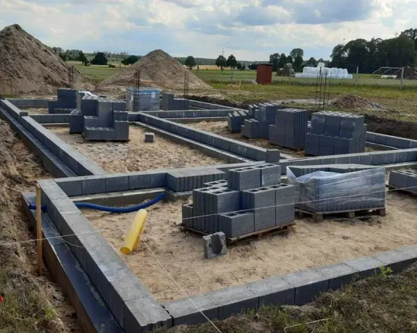 Budowa fundamentów z bloczków betonowych. Zastanawiasz się, ile kosztuje wylanie fundamentu? Na placu budowy widać materiały i postęp prac.