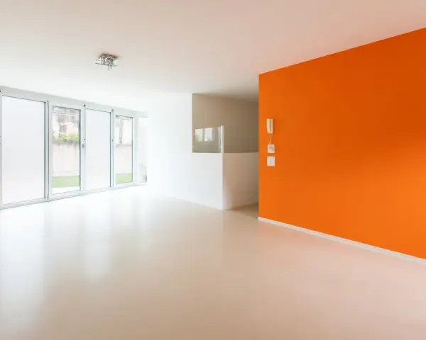 Jasne, nowoczesne wnętrze z pomarańczową ścianą i podłogą z **mikrobetonu**. Duże okna wpuszczają dużo światła.