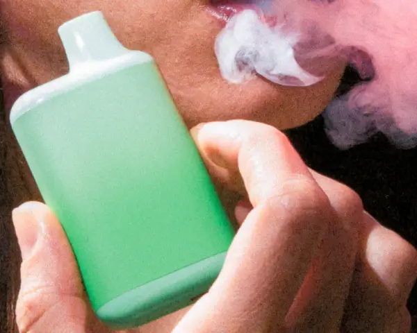 Persona vapeando un dispositivo verde, exhalando vapor. Una imagen que ilustra la diferencia entre vapear y fumar.
