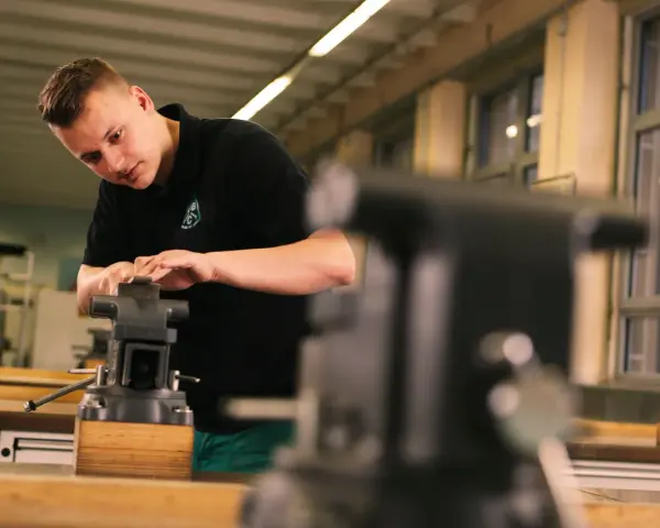 Ein junger Mann macht ein Praktikum und arbeitet konzentriert an einem Schraubstock in einer Werkstatt.