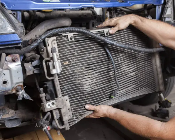 Mechanic removing a car's AC condenser, which blows hot air, for repair.