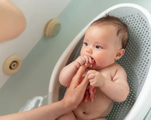 Niemowlę w wanience, rodzic sprawdza, ile stopni powinna mieć woda do kąpieli niemowlaka, by była idealna.