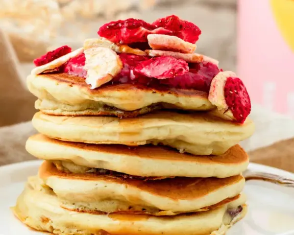 Stapel fluffiger Pfannkuchen mit gefriergetrockneten Erdbeeren und Bananen, perfekt für gesunde Snacks selber machen.