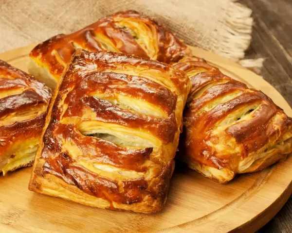 Złociste, pieczone ciasto francuskie z nadzieniem, ułożone na drewnianej desce.