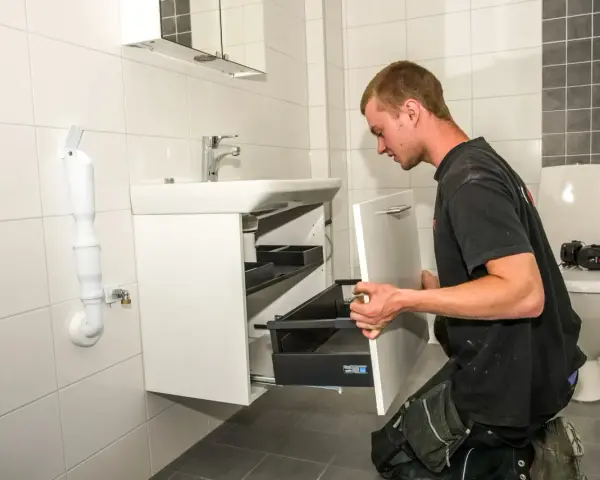 En rörmokare utför vvs arbeten i ett badrum, monterar ett nytt handfat och skåp.