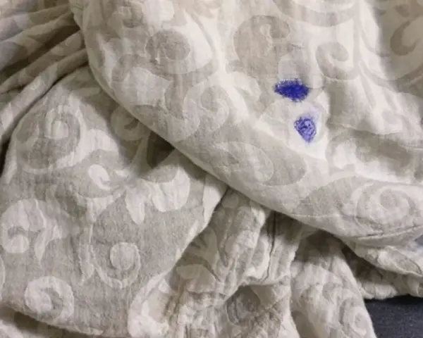 Niebieska plama po flamastrze na jasnej tkaninie z wzorem. Jak zmyć flamaster z ubrania?