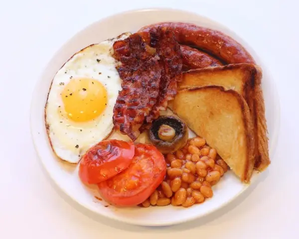 Un piatto tipico inglese con uovo fritto, bacon croccante, salsiccia, fagioli stufati, pomodori grigliati, fungo e toast.
