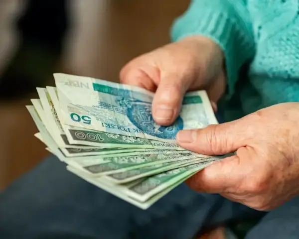 Dłonie starszej osoby liczą banknoty. Zastanawiasz się, ile wynosi dodatek do emerytury za warunki szkodliwe?