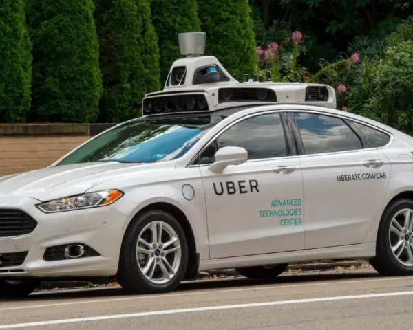 Ein weißes Uber auto mit Sensoren auf dem Dach fährt auf einer Straße.