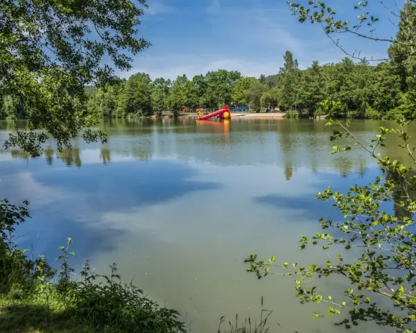 Idyllischer sulzfeld badesee mit Spielplatz und Rutsche, umgeben von grünen Bäumen.