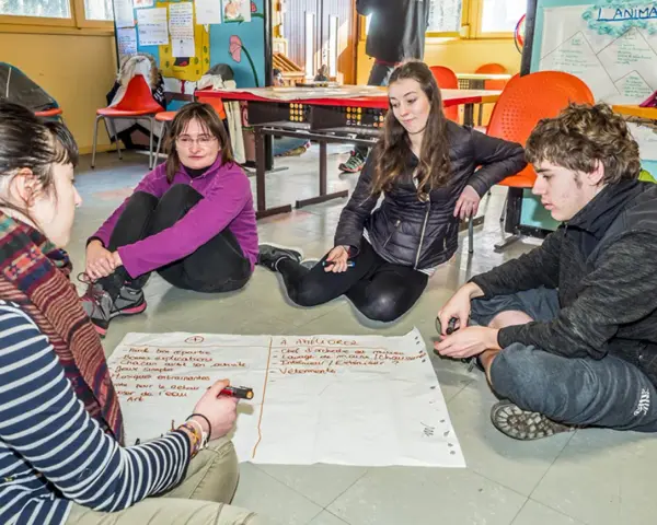 Quatre jeunes discutent autour d'un papier, participant à un mouvement d'éducation populaire. Ils brainstorment des idées pour améliorer une activité.