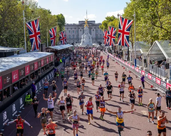 Tysiące biegaczy na trasie maratonu londyn, z flagami Wielkiej Brytanii i Pałacem Buckingham w tle.