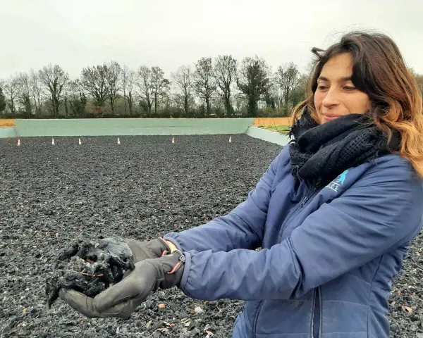 Une femme tient dans ses mains un échantillon de fibre, un avis carrière en fibre. L'arrière-plan montre une carrière équestre.