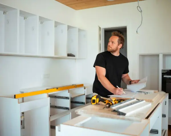 Mężczyzna planuje, jak zabudować przestrzeń nad szafkami kuchennymi, analizując projekt.