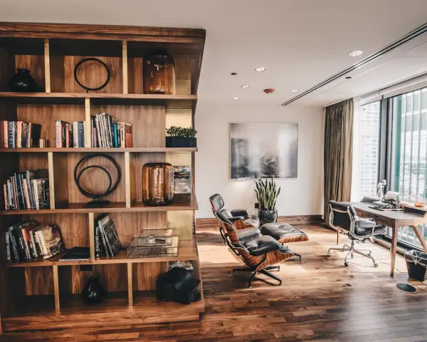 Drewniana biblioteczka z książkami i dekoracjami, obok skórzane fotele i biurko z maszyną do pisania. Styl **modern rustic**.