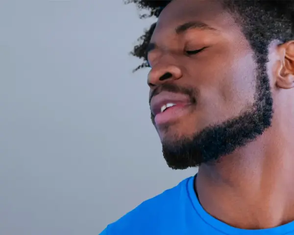 Hombre con barba cortina y cabello afro, ojos cerrados, con expresión de paz.