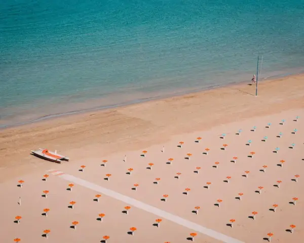 Pusta plaża w Rimini z rzędami pomarańczowych parasoli i łodzią ratowniczą.