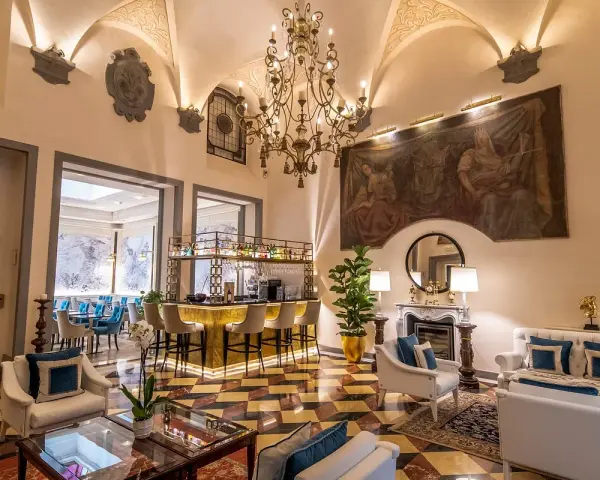 Elegant hotel lounge with a bar, fireplace, ornate chandelier, and artwork.
