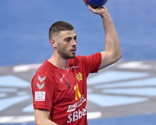 Branko Vujović, zawodnik piłki ręcznej, w czerwonej koszulce z numerem 11, trzyma piłkę nad głową.