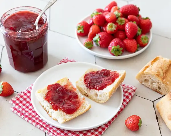 Un pot de confiture de fraise maison, des tartines de pain frais garnies de cette confiture, et des fraises fraîches. Un délice !