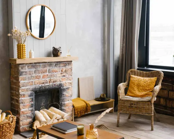 Un camino di mattoni rustico, pronto per essere rinnovato. Legna accatastata, decorazioni e una sedia in vimini invitano al relax.
