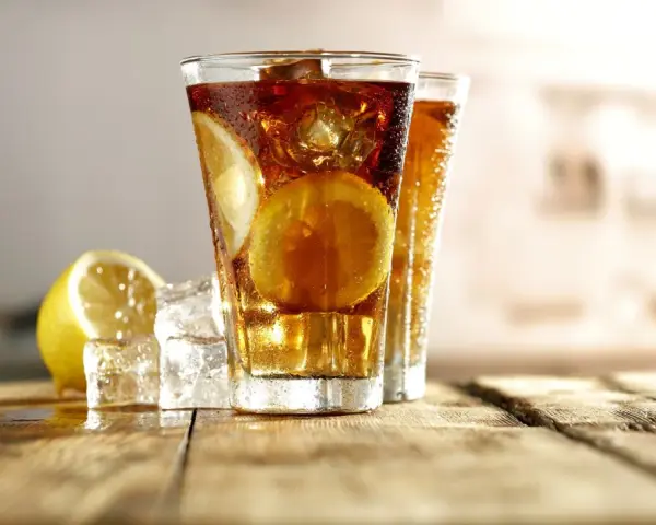 Dwa orzeźwiające drinki Long Island Iced Tea z plasterkami cytryny i lodem na drewnianym blacie.